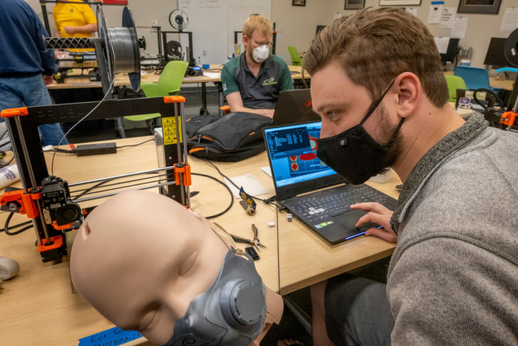 Eric Schneider, a senior aerospace engineering student at Missouri S&T, tests the fit of a prototype 3-D printed surgical mask on the head of a mannequin in the Kummer Student Design Center at S&T. In the background is Stephen Williams, an S&T mechanical engineering student. The university is helping Phelps Health prepare for coronavirus patients by 3-D printing masks and face shield brackets. Photo by Tom Wagner/Missouri S&T.