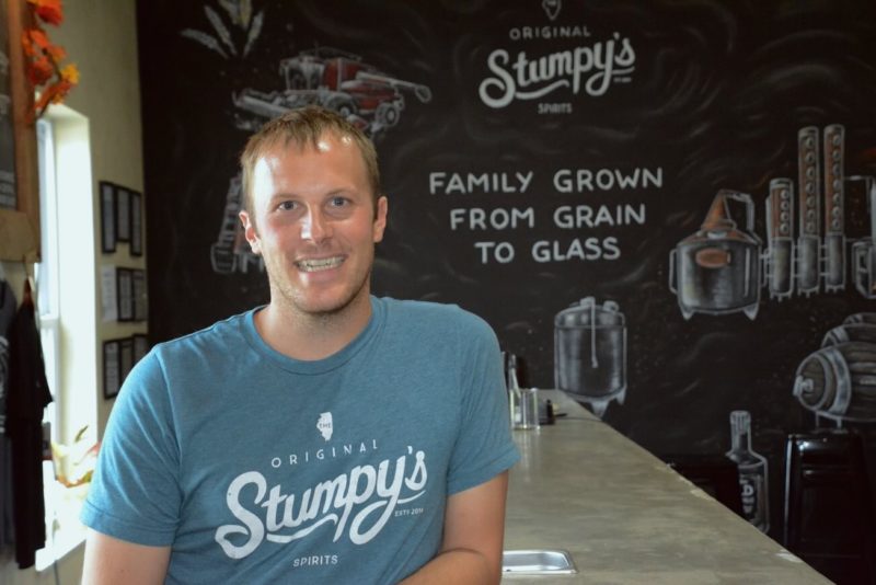 Photo of Adam Stumpf in front of signs that reads, "Family grown from grain to glass"