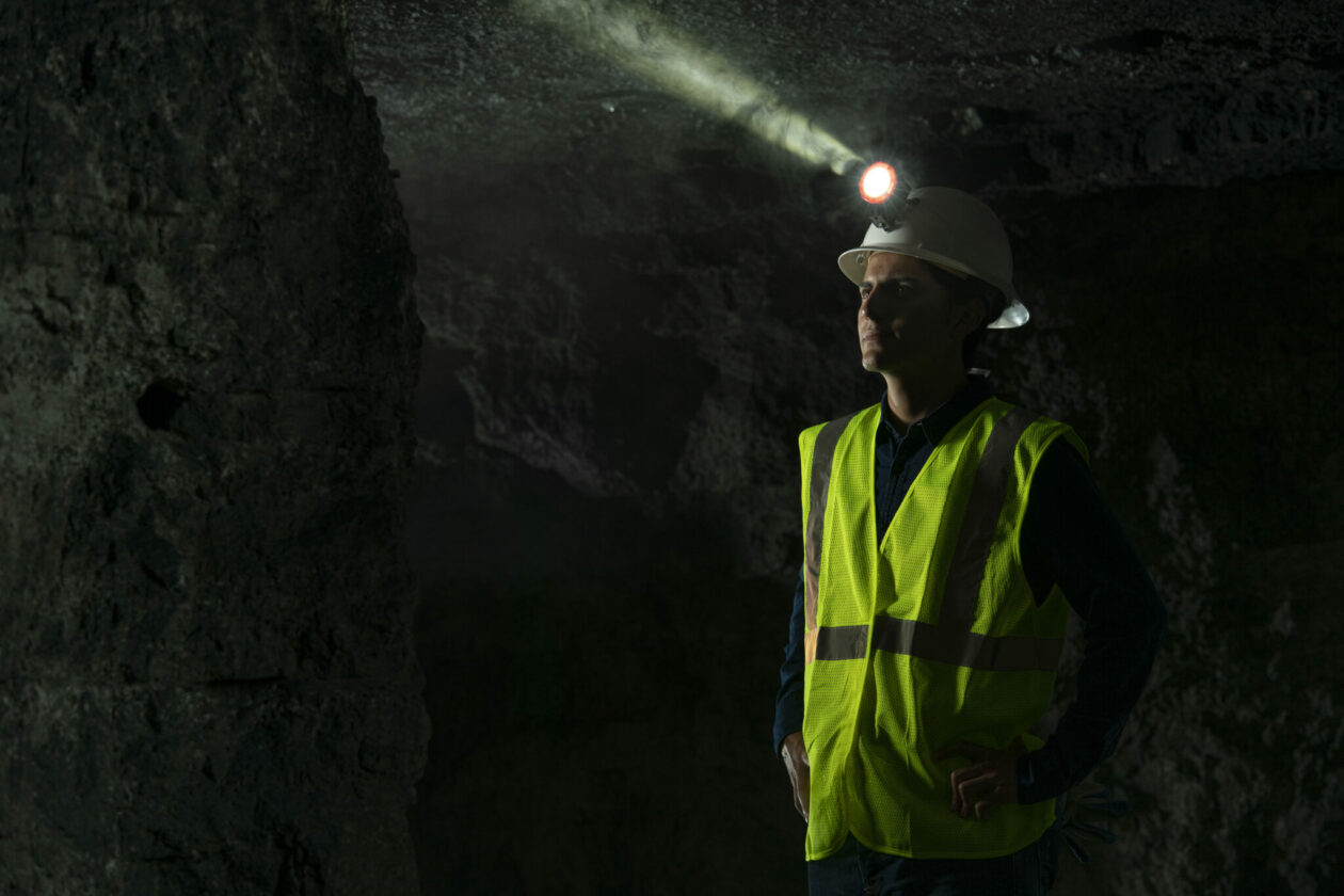 Young man in yellow safety vest and head lamp standing in a dark mine