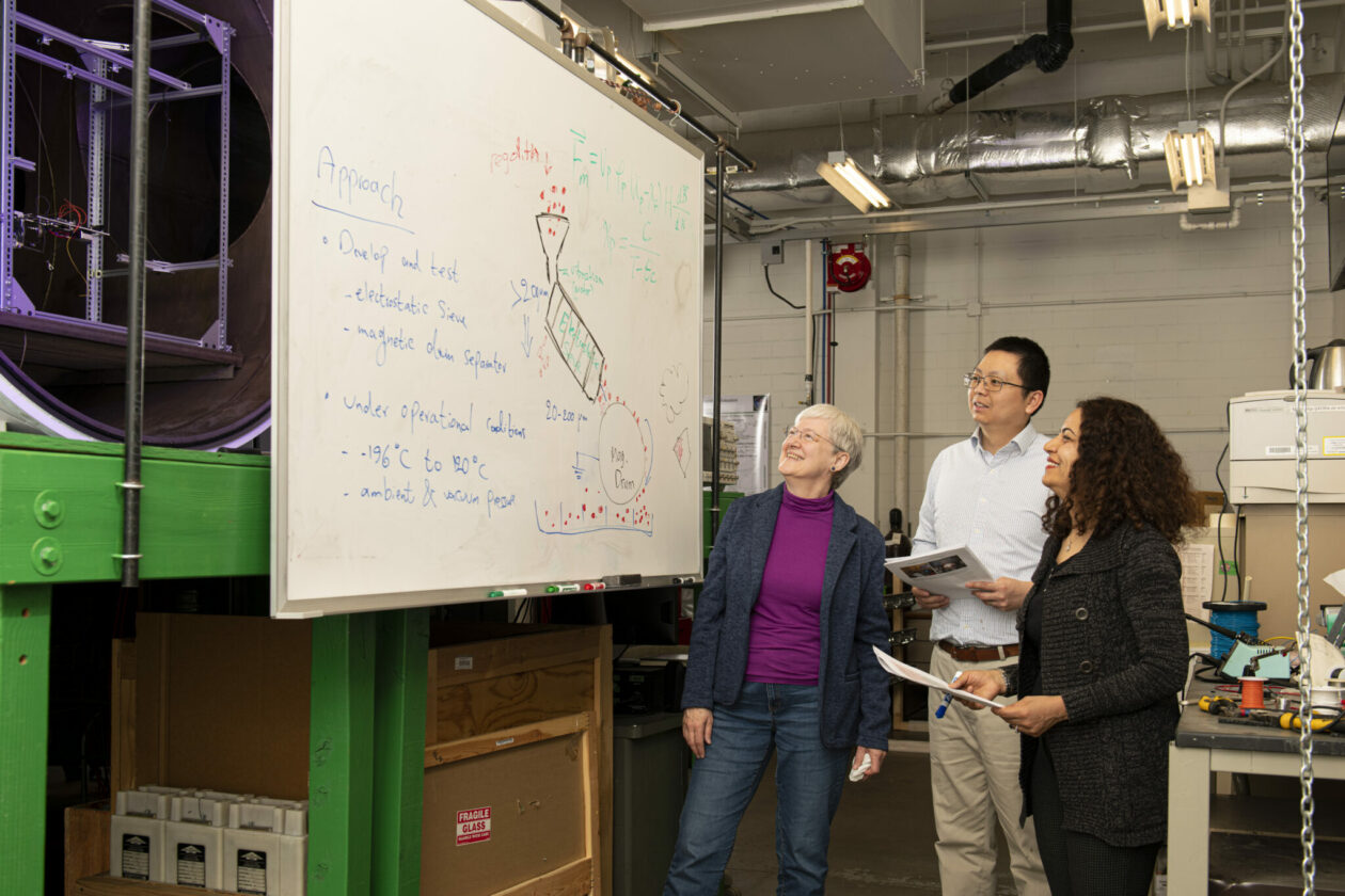 Photo of Dr. Leslie Gertsch, Dr. Frank Han and Dr. Fateme Rezaei looking at models drawings on white board