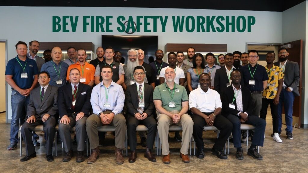 Wprkshop participants in two rows, one behind the other, in a photo with a banner reading "BEV Fire Safety Workshop" in green letter on a white background.