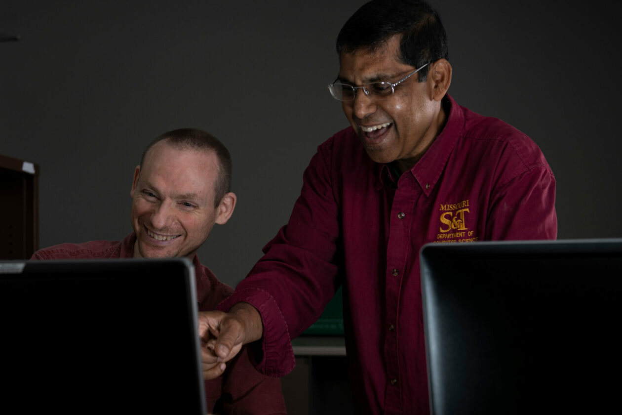 Man in maroon shirt with student at computer