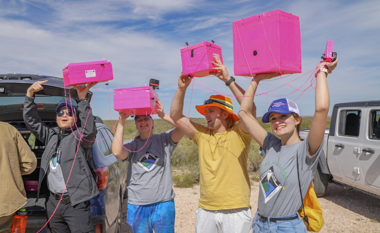 Team members holding pink satellites