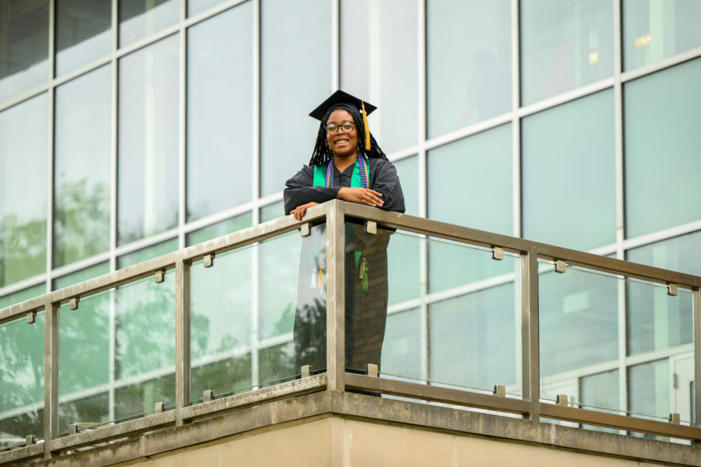 Jennifer Onoh in cap and gown standing on Toomey Hall balcony on S&T's campus.