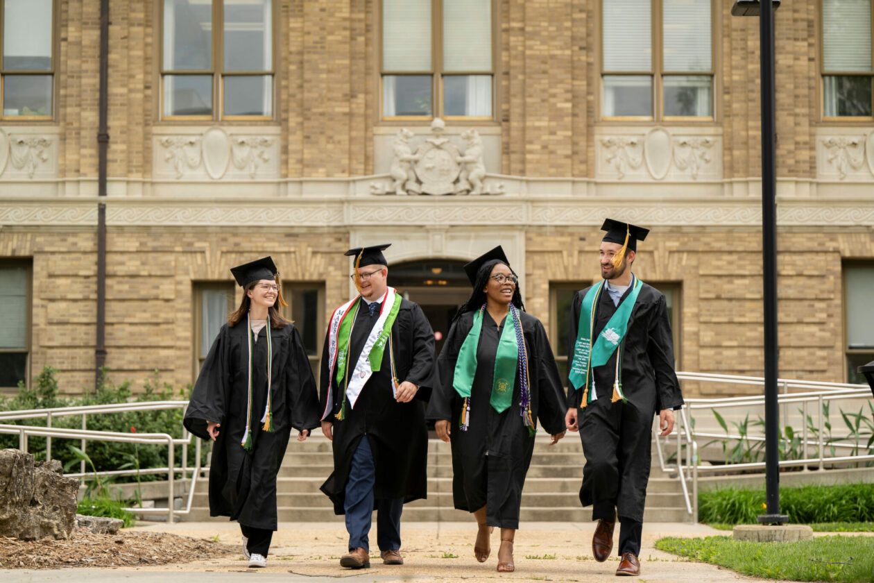 Four S&T graduates in caps and gown outside Norwood Hall on S&T campus