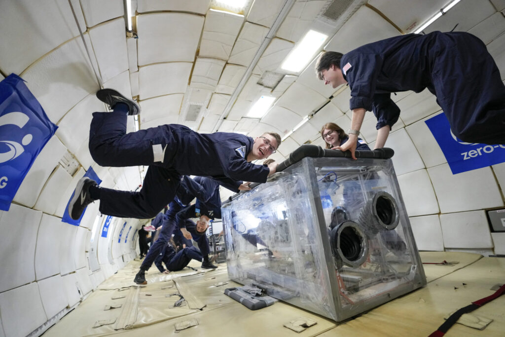 Joshua Eiter, Marissa Verduin, and Trey Brown hold the box containing their technology, while Justin Viers floats upside down behind them. Photo courtesy of Zero Gravity Corp.