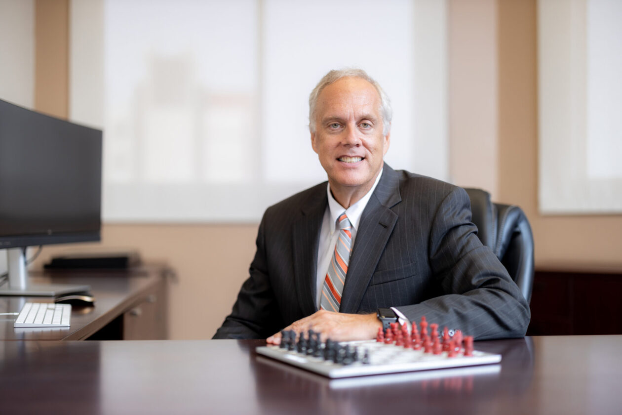 Man in suit sits at desk with chess board in foreground