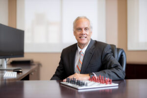 Man in suit sits at desk with chess board in foreground