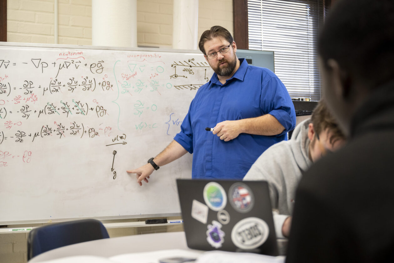 Dr. Joshua Schlegel teaches S&T students in a classroom, pointing at calculations on a whiteboard.