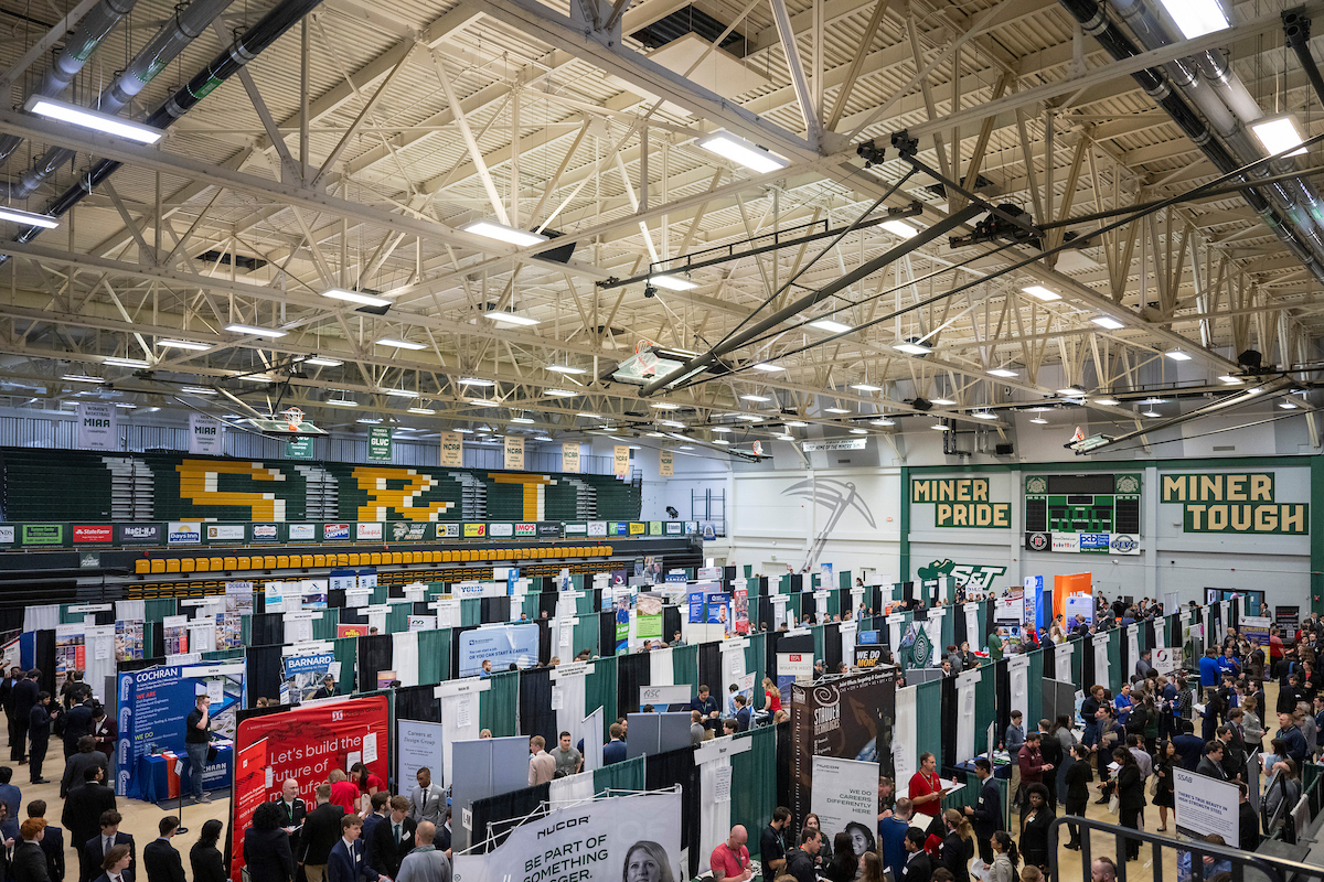 Scene of large career fair with employer booths and people throughout gymnasium