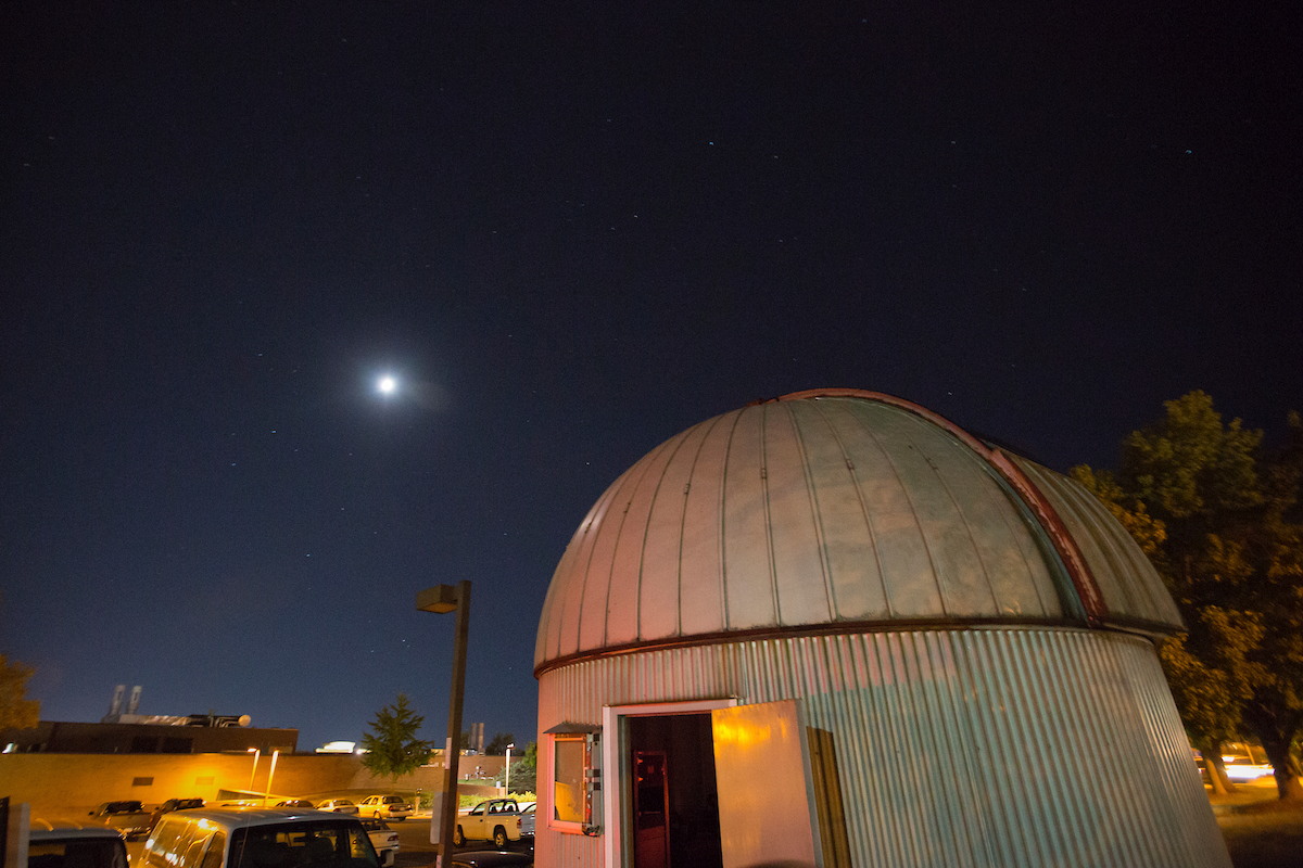 The Missouri S&T Observatory, a circular grey building with a domed roof, against a background of the night sky with a full moon.