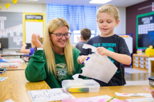 Greycen teaching elementary school student how to use scissors.
