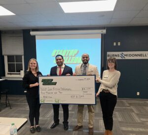 Four people gather around a large check at the S&T Startup Challenge.