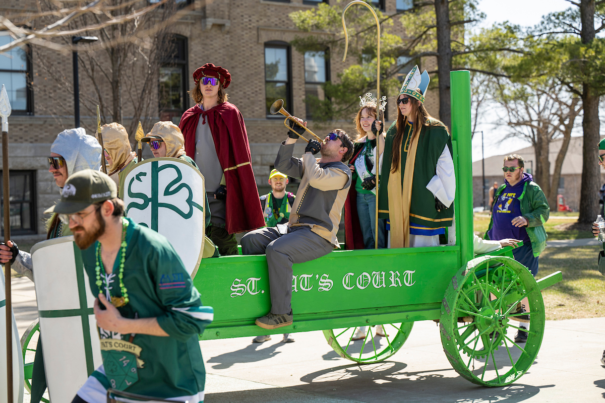 Students in costume as St. Pat and his court arrive on campus in a bright green cart.