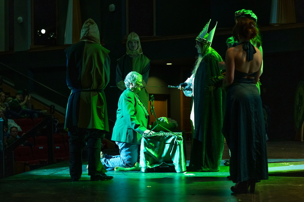 An honoree kneels on the Leach Theater stage to be knighted during St. Pat's coronation.