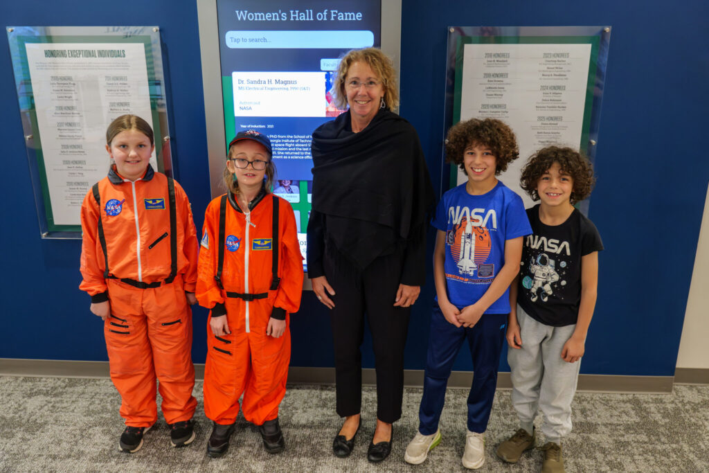 Children with Sandra Magnus. Two wear orange astronaut costumes. Two wear NASA T-shirts.