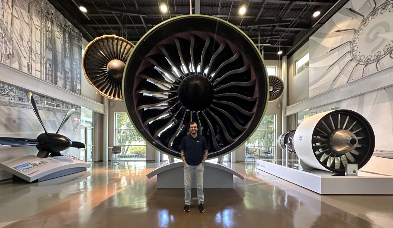 Logan Wilcox in front of a plane engine at GE Aerospace.