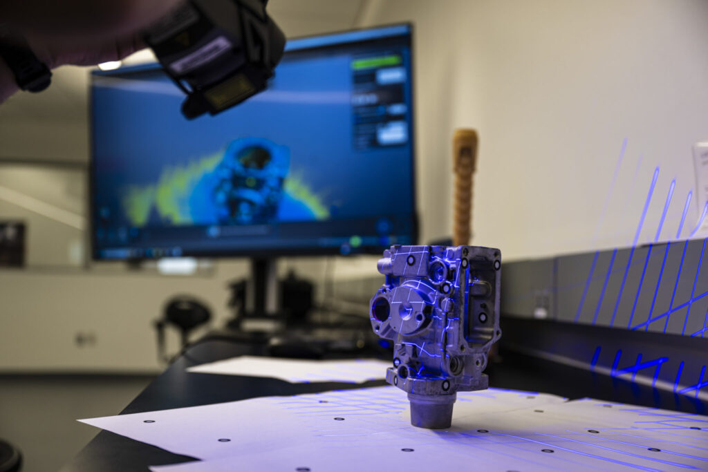 A 3D scanning system projects patterned blue light onto a metal part to capture precise measurements. 