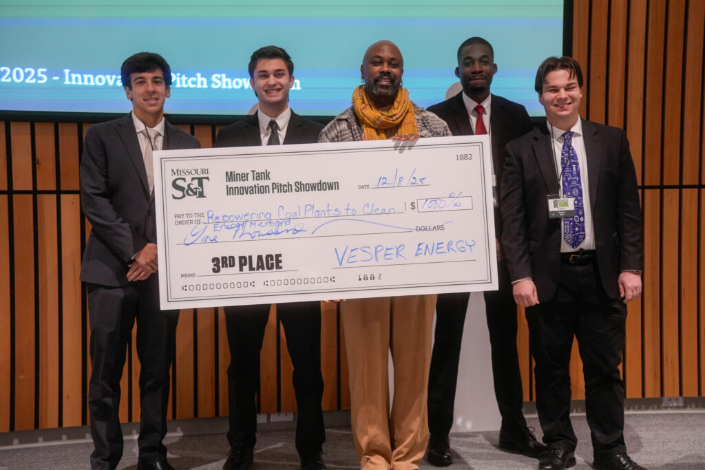 A group photo of Vieira's team during the Miner Tank Innovation Showdown. There are five people holding a large check for 1,000 dollars. The check reads: "Missouri S&T. Miner Innovation Pitch Showdown. Date 12/8/25. Pay to the order of: Repowering Coal Plants to Clean. Memo: third place. Vesper Energy."