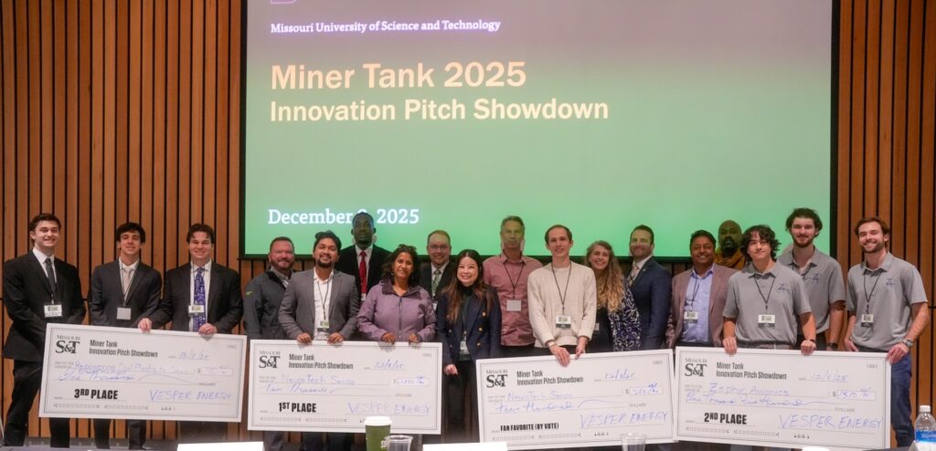 All teams pose for a photo at the 2025 Miner Tank Innovation Pitch Showdown. Multiple groups of people are holding large checks. The background is a large screen that says "Missouri University of Science and Technology. Miner Tank 2025 Innovation Pitch Showdown. December 2025."