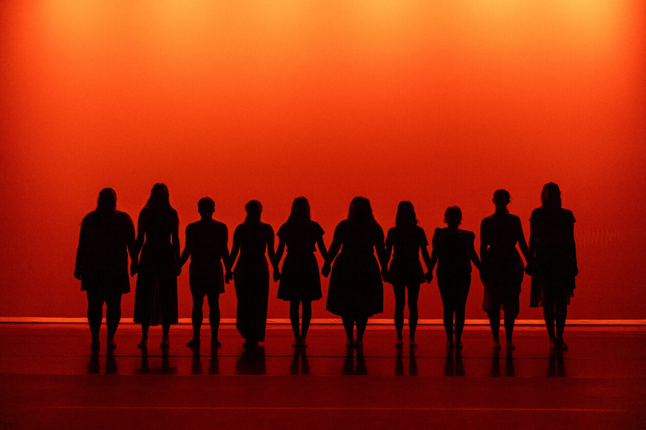 Silhouettes of students on the Leach Theatre stage, backlit in orange.
