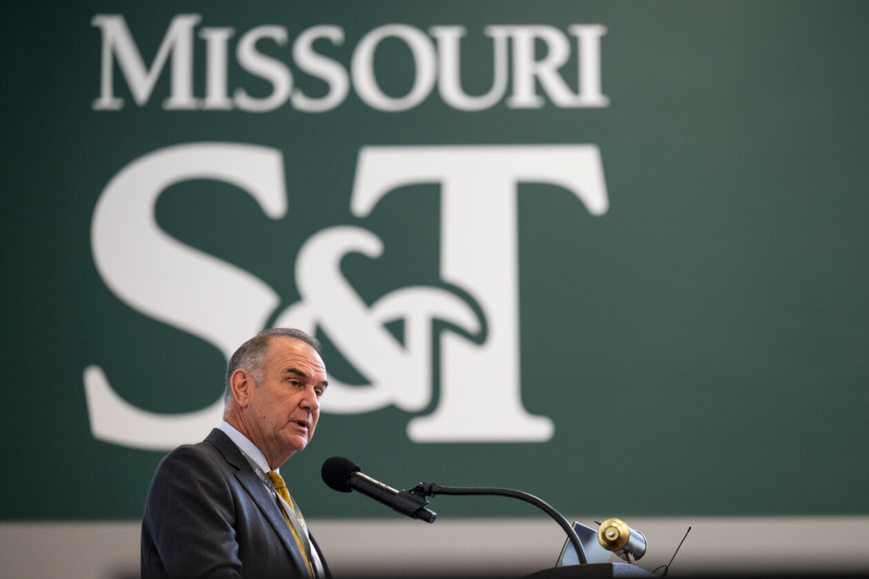 Governor at microphone. Large Missouri S&T logo in background.