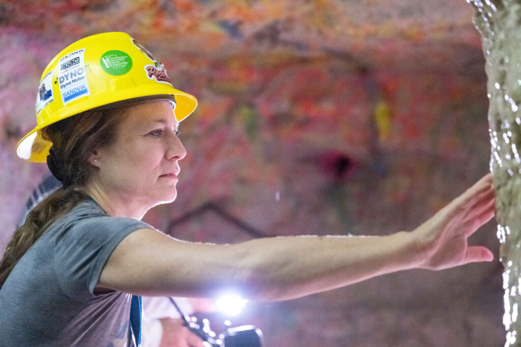 Woman in hard hat touches wall of cave.
